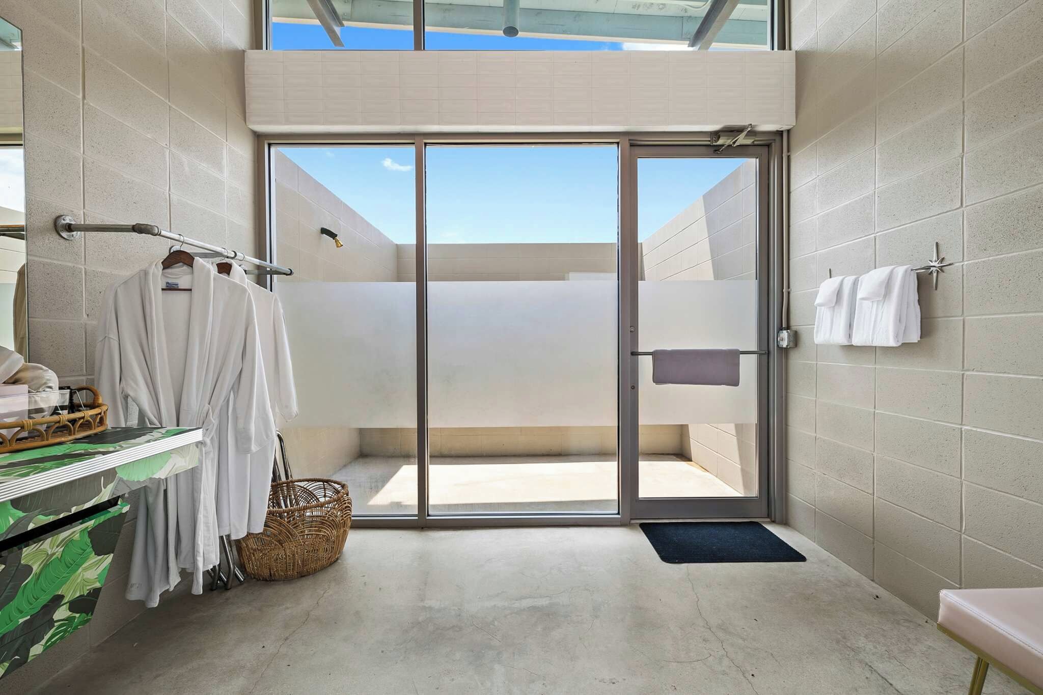 Une salle de bain moderne avec une porte en verre donnant sur un espace extérieur, un porte-serviettes et un panier en osier.