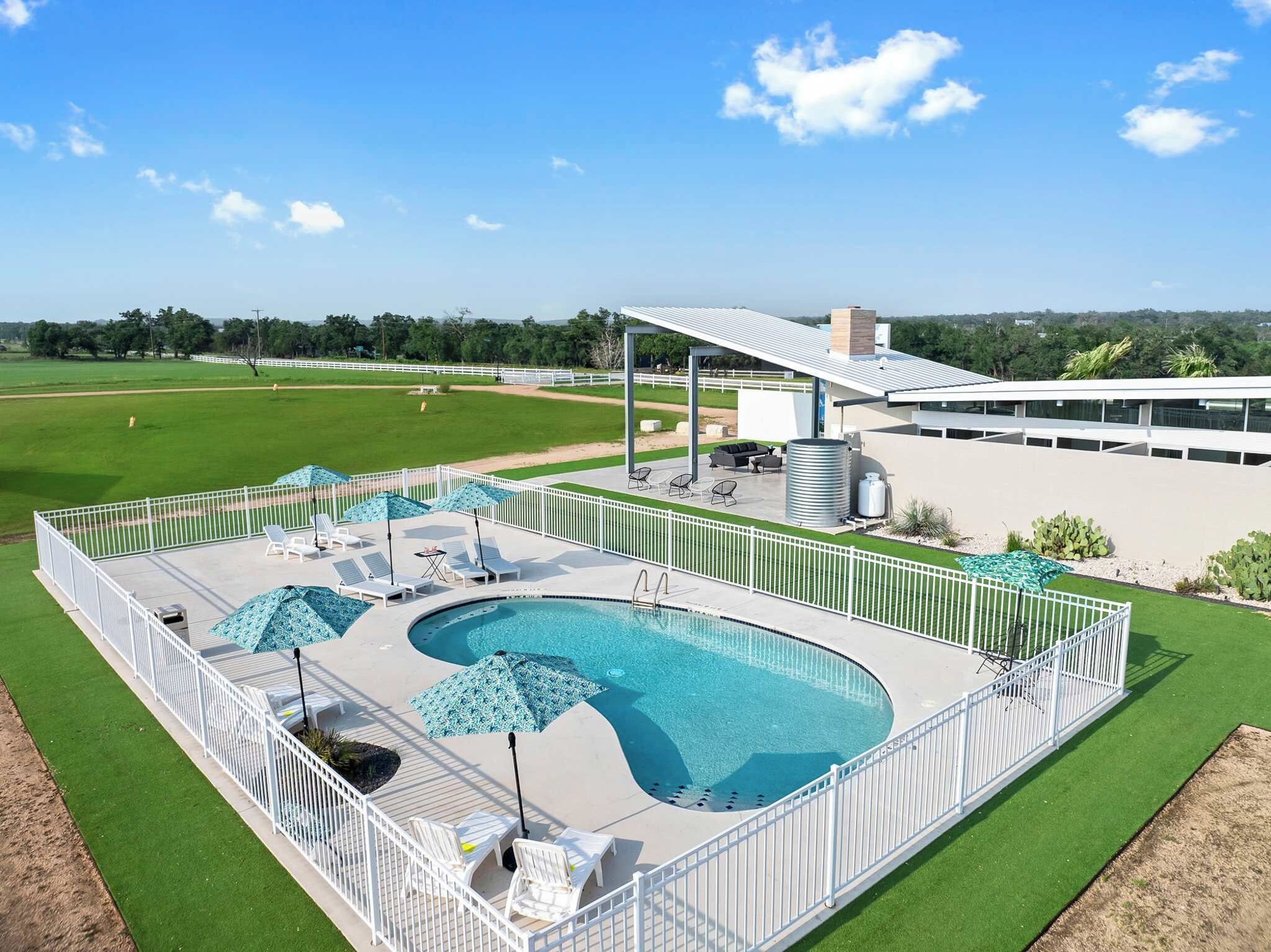 Un espace piscine comprenant deux piscines distinctes, entouré d’une clôture blanche, et un coin salon abrité.
