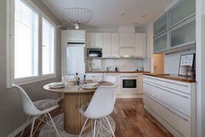 Eine moderne Küche mit weißen Schränken, einer zentralen Kochinsel mit Sitzgelegenheiten und einem Essbereich mit weißen Stühlen.