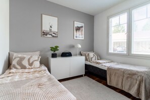 Ein Schlafzimmer mit zwei Einzelbetten, einem weißen Kleiderschrank, einem Schreibtisch mit Pflanze und zwei gerahmten Bildern an der Wand.