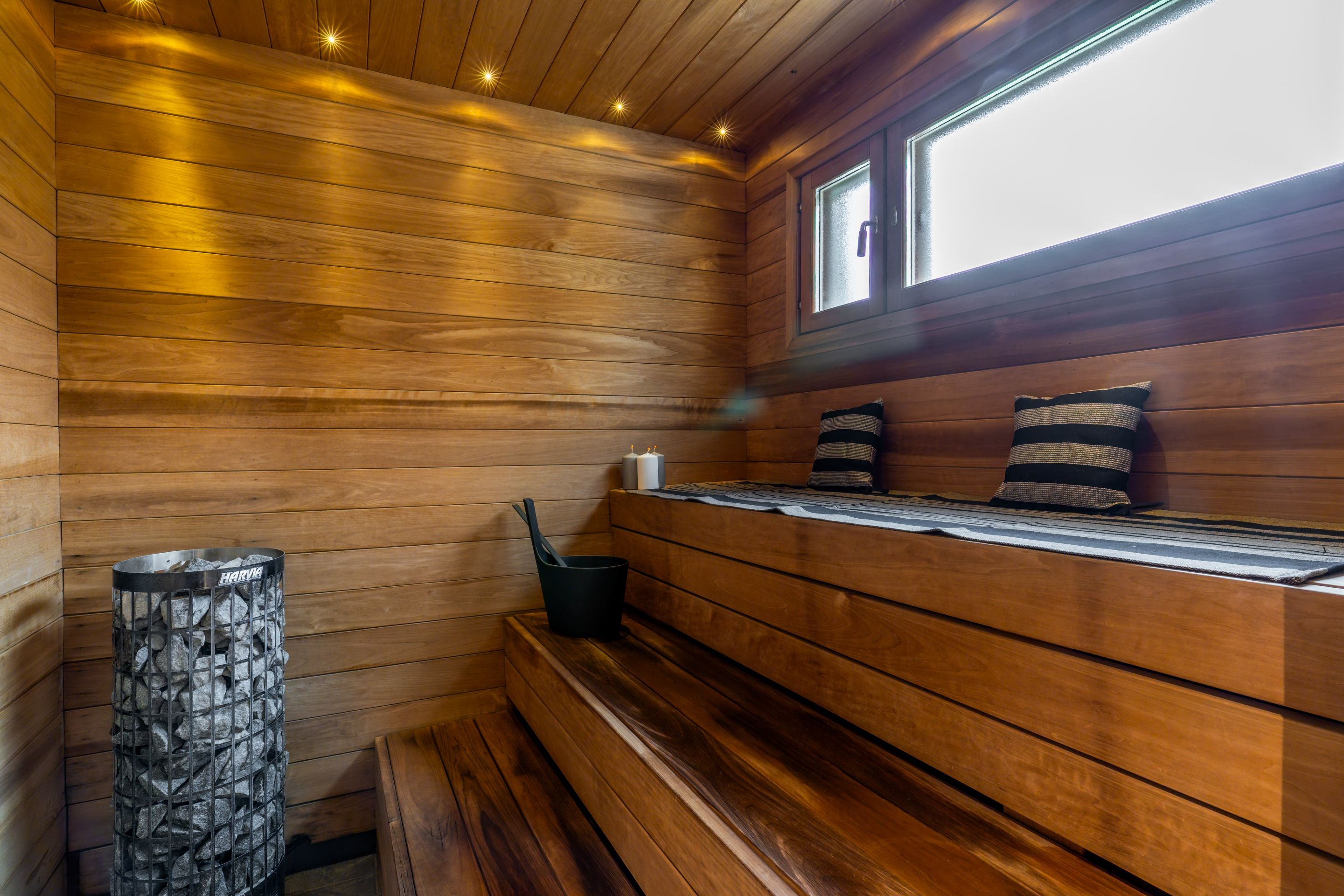 Een sauna met houten wanden, een bank, een stenen bak en een raam.
