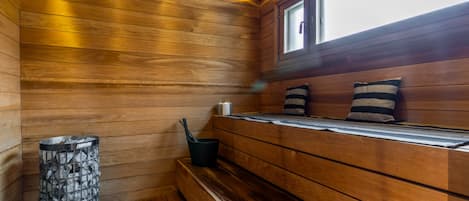 Un sauna avec des murs en bois, un banc, un récipient en pierre et une fenêtre.
