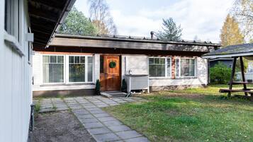 A single-story house with a front door, a small porch, and a covered outdoor seating area.