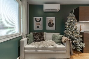 A living room with a sofa, a Christmas tree, and artwork on the wall. - Santa's Star Residence - Grand Apartment (Rovaniemi)