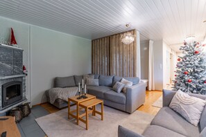 A modern living room with a fireplace, a grey sofa, a wooden coffee table, and a Christmas tree. - Santa's Star Residence - One-bedroom Suite (Rovaniemi)