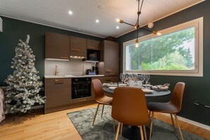 A modern kitchen with wooden cabinets, a built-in oven, and a dining area with a round table and chairs. - Santa's Star Residence - One-bedroom Suite (Rovaniemi)