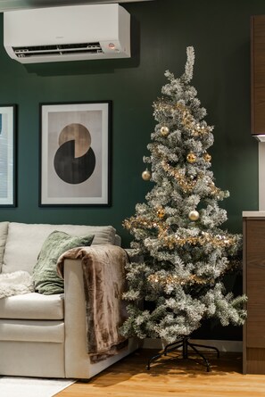 A living room with a white couch, a small Christmas tree, and a framed picture on the wall. - Santa's Star Residence - One-bedroom Suite (Rovaniemi)