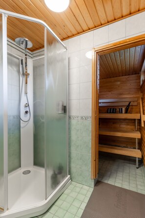 A shower with a glass door, a wooden ceiling, and a tiled floor. - Santa's Star Residence - One-bedroom Suite (Rovaniemi)