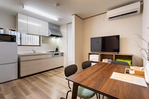 A compact kitchen with modern appliances, a dining area with a wooden table, and a flat-screen TV. - U-neighbor Noda (Osaka, Fukushima-ku)