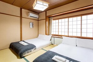 A traditional Japanese-style room with tatami flooring, two beds with white bedding, a large window with a view, and a ceiling fan. - U-neighbor Noda (Osaka, Fukushima-ku)