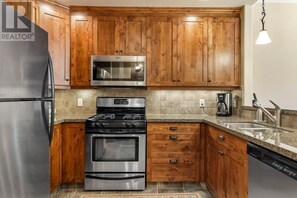 A kitchen with wooden cabinets, stainless steel appliances, a granite countertop, and a dishwasher. - Woodhaven #34 | 3 Peaks Rentals (Sun Peaks)