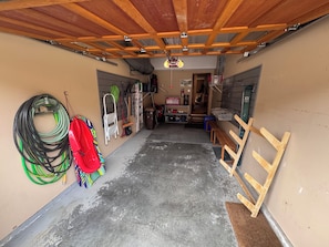 A garage with a concrete floor, wooden beams on the ceiling, and various tools and equipment. - Woodhaven #34 | 3 Peaks Rentals (Sun Peaks)