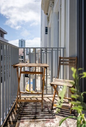 A balcony with a wooden table and chair, a white railing, and a view of the cityscape. - Nando's Place 1 - Charming 1BR Apt near Old San Juan and Beach (San Juan)