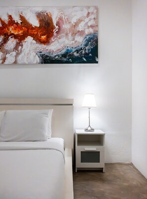 Ein Hotelzimmer mit Bett, Nachttisch mit Lampe und einem großen, abstrakten Gemälde an der Wand.