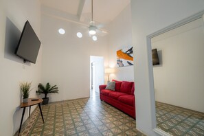 A hallway with a red sofa, a TV mounted on the wall, a ceiling fan, and patterned flooring. - Nando's Place 3 - Charming 1BR Apt near Old San Juan and Beach (San Juan)