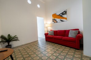 A red sofa with patterned cushions, a potted plant, and a tiled floor with a geometric design. - Nando's Place 3 - Charming 1BR Apt near Old San Juan and Beach (San Juan)