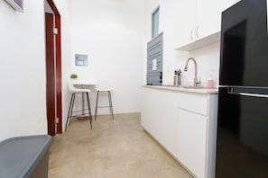 A compact kitchen with white cabinets, a black refrigerator, a sink with a faucet, and two stools. - Nando's Place 4 - Charming 1BR Apt near Old San Juan and Beach (San Juan)