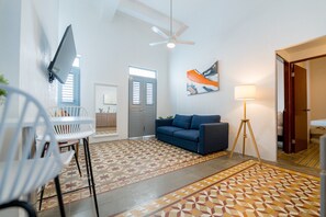 Ein modernes Wohnzimmer mit einer Couch, einem an der Wand befestigten Fernseher, einem Deckenventilator und einer Stehlampe.