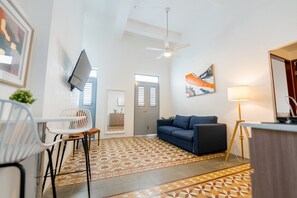 Een moderne woonkamer met een bank, een aan de muur bevestigde televisie, een plafondventilator en een vloer met een patroon.