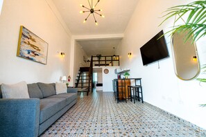 A modern living room with a grey sofa, a patterned floor, a staircase, a dining area, and a TV mounted on the wall. - Elokut Loft 2 - Steps from Old San Juan and Escambron Beach (San Juan)