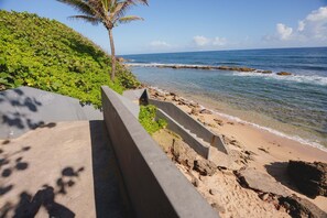 A concrete barrier with a palm tree and greenery beside a beach with clear blue water. - Elokut Loft 6 - Steps from Old San Juan and Escambron Beach (San Juan)