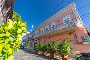 Un edifici rosa amb un balcó, plantes en testos i línies elèctriques visibles.