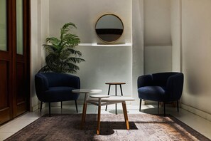 Una habitación con dos sillones azul oscuro, una mesita redonda y un espejo grande en la pared.