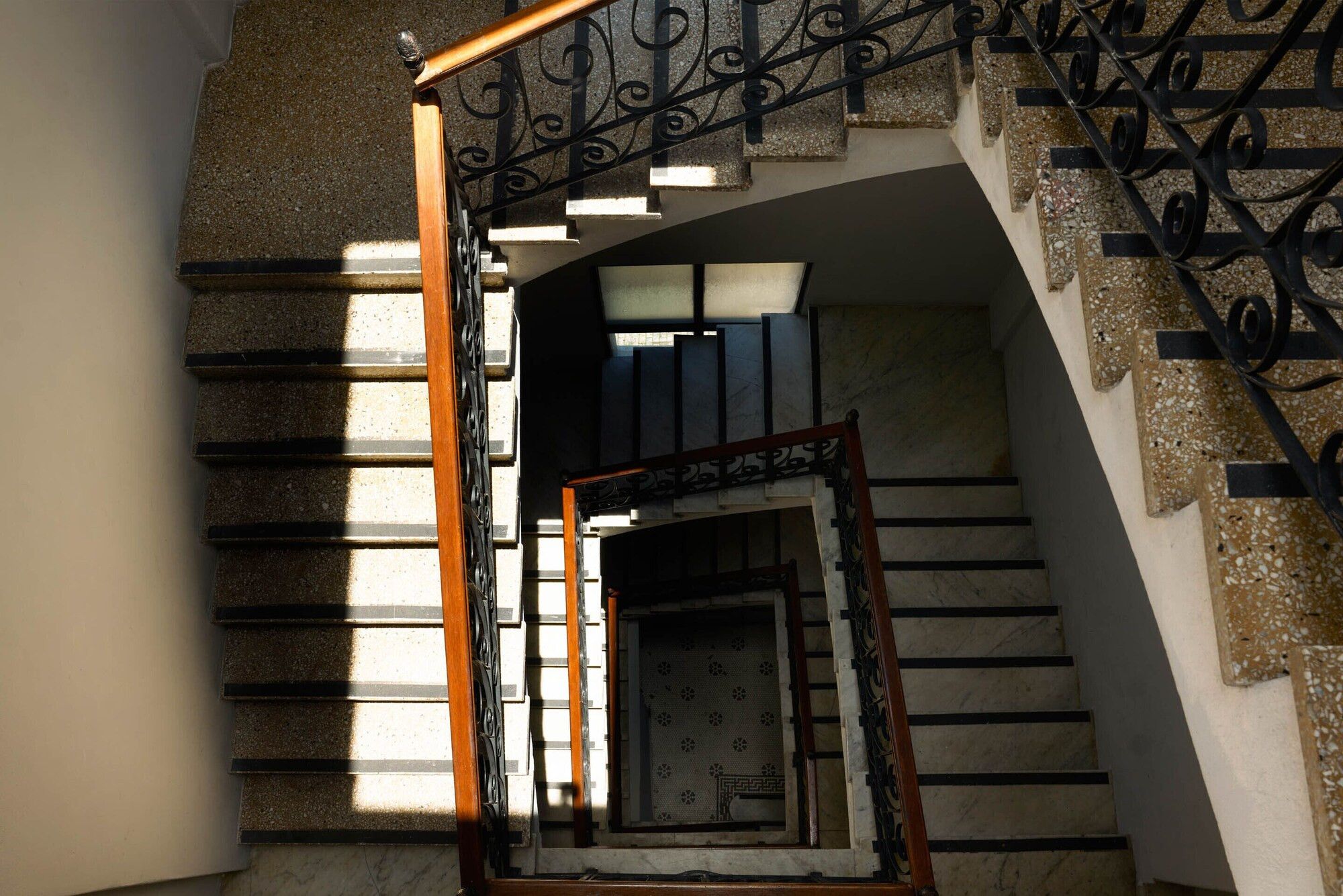 A staircase with a wooden handrail and black metal balusters, leading to a landing with a patterned door.