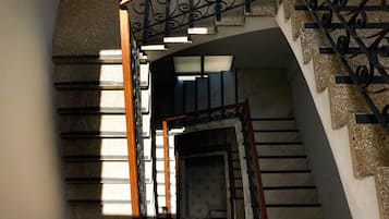 A staircase with a wooden handrail and black metal balusters, leading to a landing with a patterned door.