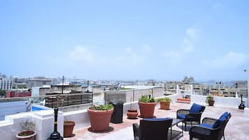 Terraza en la azotea con mobiliario exterior, plantas en macetas y vistas a la ciudad.