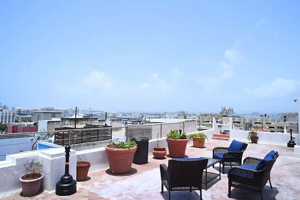 Terraza en la azotea con mobiliario exterior, plantas en macetas y vistas a la ciudad.
