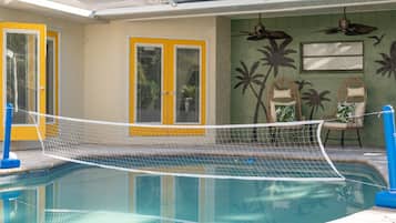 Una piscina con zona delimitada por una red, una puerta con paneles de vidrio y un muro con murales de palmeras.
