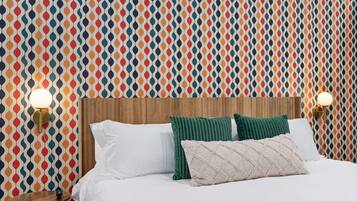 Una cama con ropa de cama blanca, dos almohadas verdes y un cabecero de madera. Hay dos lámparas de pared a ambos lados de la cama.