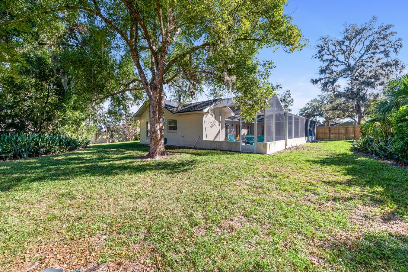 A house with a covered patio, a lawn, and a large tree in the foreground.
