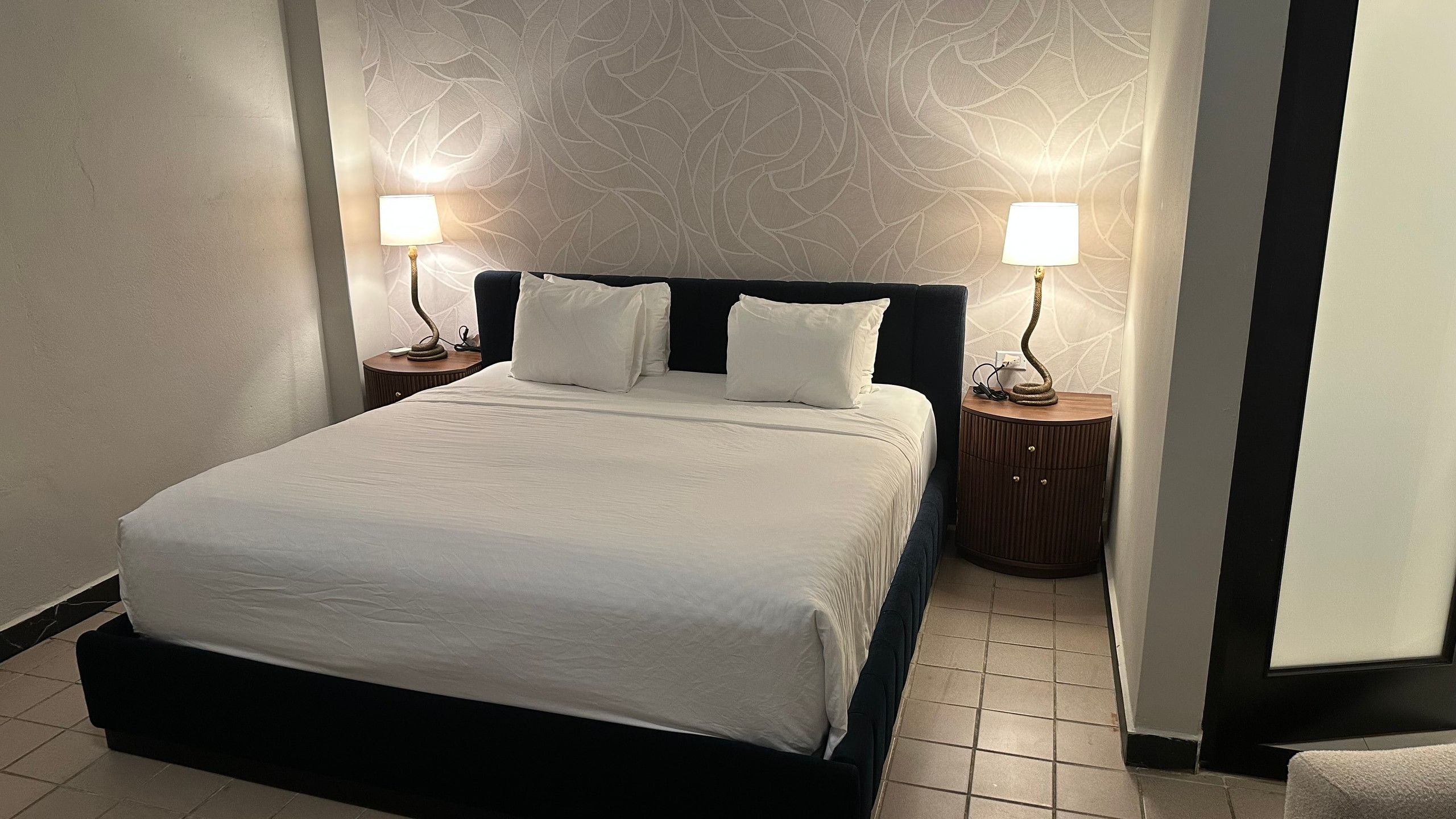 A neatly made bed with white linens, two bedside tables with lamps, and a patterned wall behind.