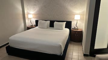 Una cama bien hecha con sábanas blancas, dos mesitas de noche con lámparas, y un papel tapiz estampado en la pared.