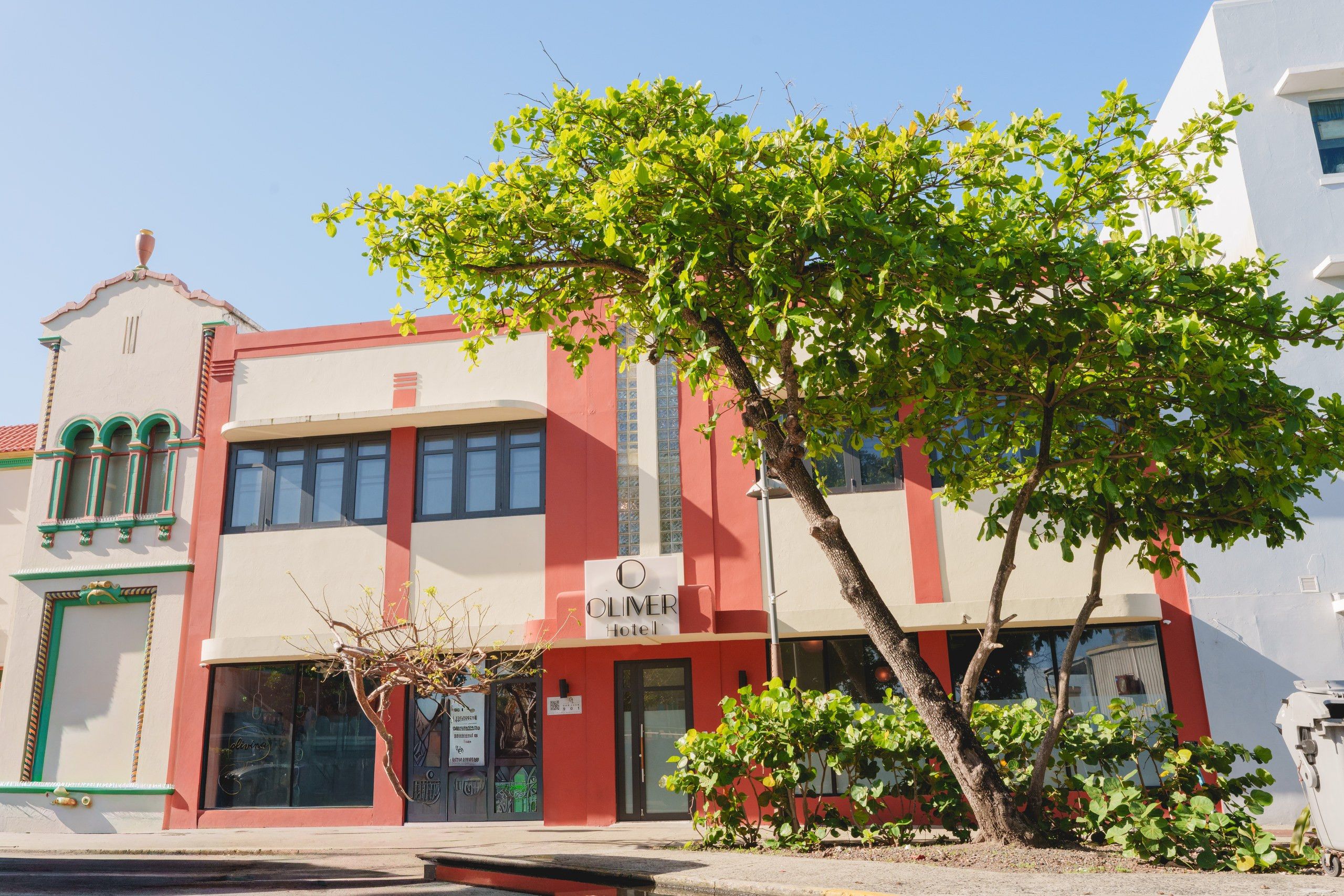 Un hôtel avec une façade rouge et blanche, une enseigne et un arbre devant.