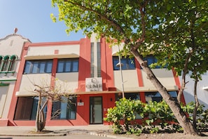 A hotel building with a red and white facade, a sign indicating it is a hotel, and a tree in the foreground.