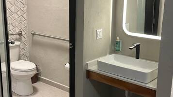 Un baño con inodoro blanco, lavamanos con espejo y un perchero para toallas.