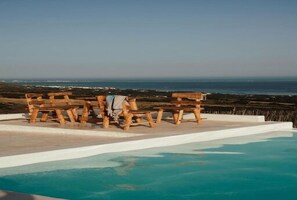 Una piscina con bancos de madera y vista al océano.