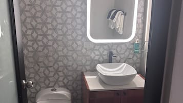 Un baño con inodoro, lavamanos, espejo y toallero.
