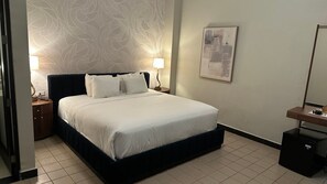 A hotel room with a bed, nightstands, a lamp, a painting, and a desk with a computer. - The Oliver, Deluxe Room with King Bed, Old San Juan (San Juan)
