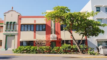 Un hotel con fachada roja y blanca, un letrero y un árbol en primer plano.