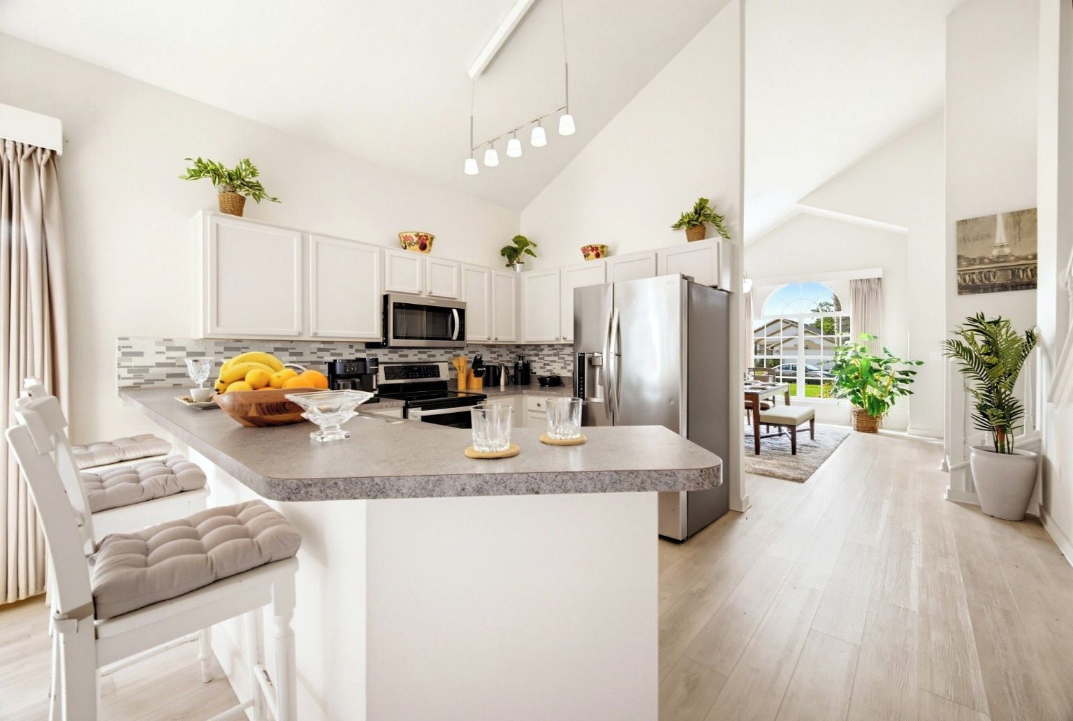 A modern kitchen with white cabinetry, stainless steel appliances, and a central island with a bowl of fruit.