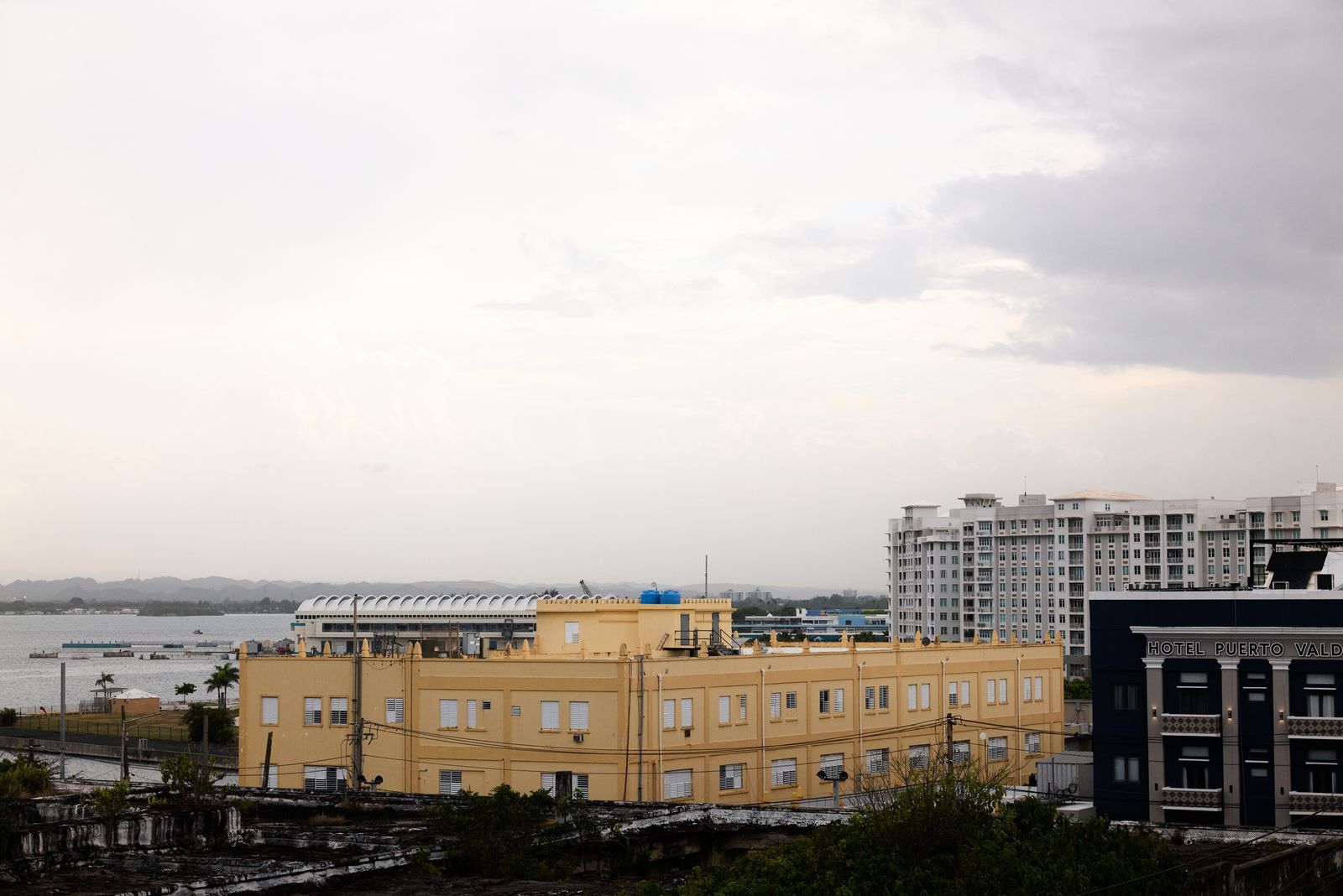 Une vue urbaine d’une ville côtière, avec un imposant bâtiment jaune et un hôtel appelé « HÔTEL PUERTO VALD ».