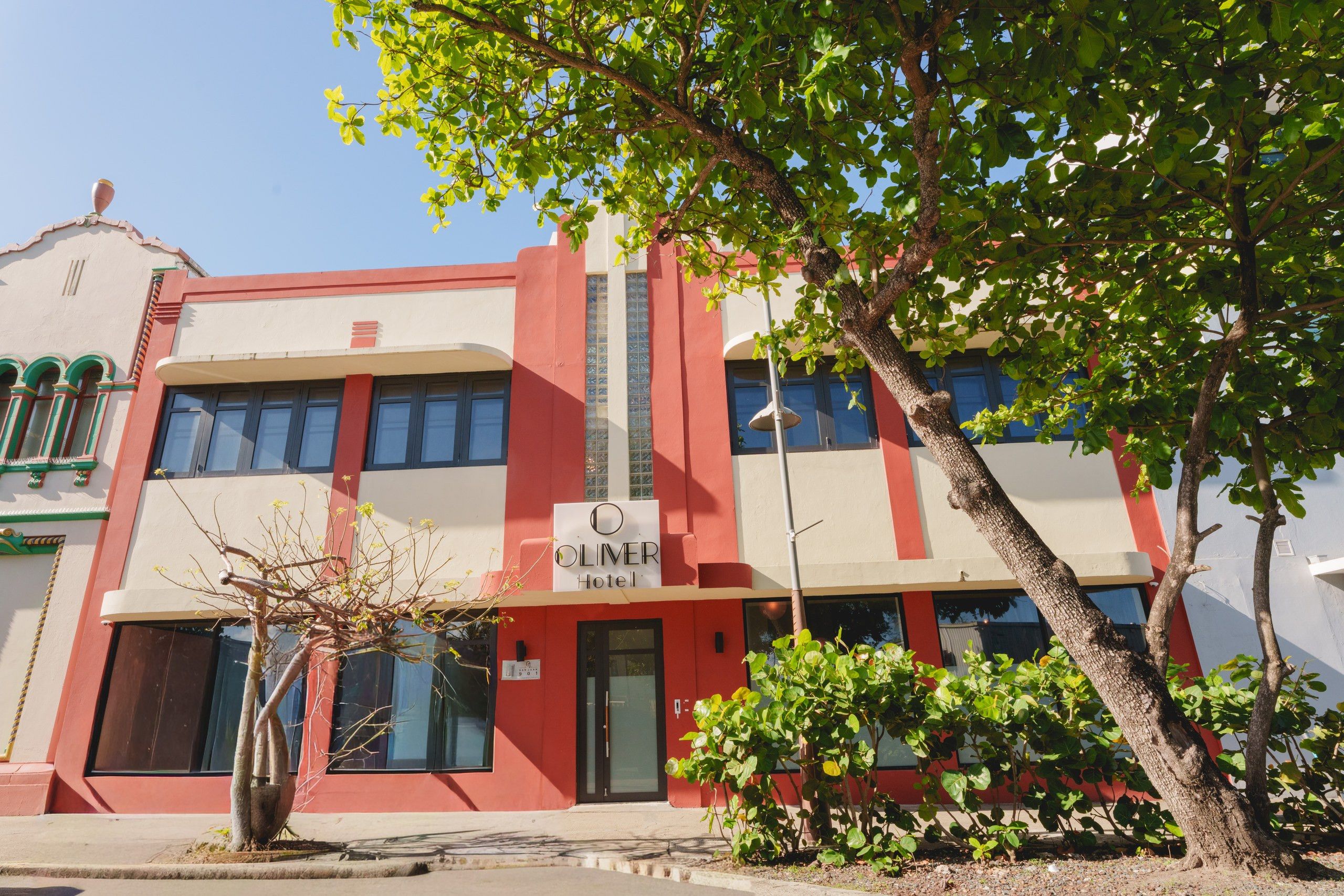 A hotel building with a red and white facade, a sign indicating it is a hotel, and a tree in the foreground.