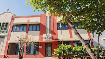 Un edificio de hotel con fachada roja y blanca, un cartel que indica que es un hotel y un árbol en primer plano.