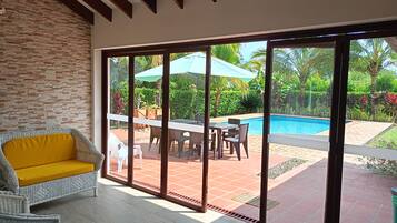 A room with a view of a swimming pool, a dining area with outdoor furniture, and a large sliding glass door.