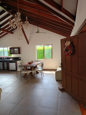 A spacious dining area with a high ceiling, a chandelier, and a view of greenery outside. - New Listing (Meta)