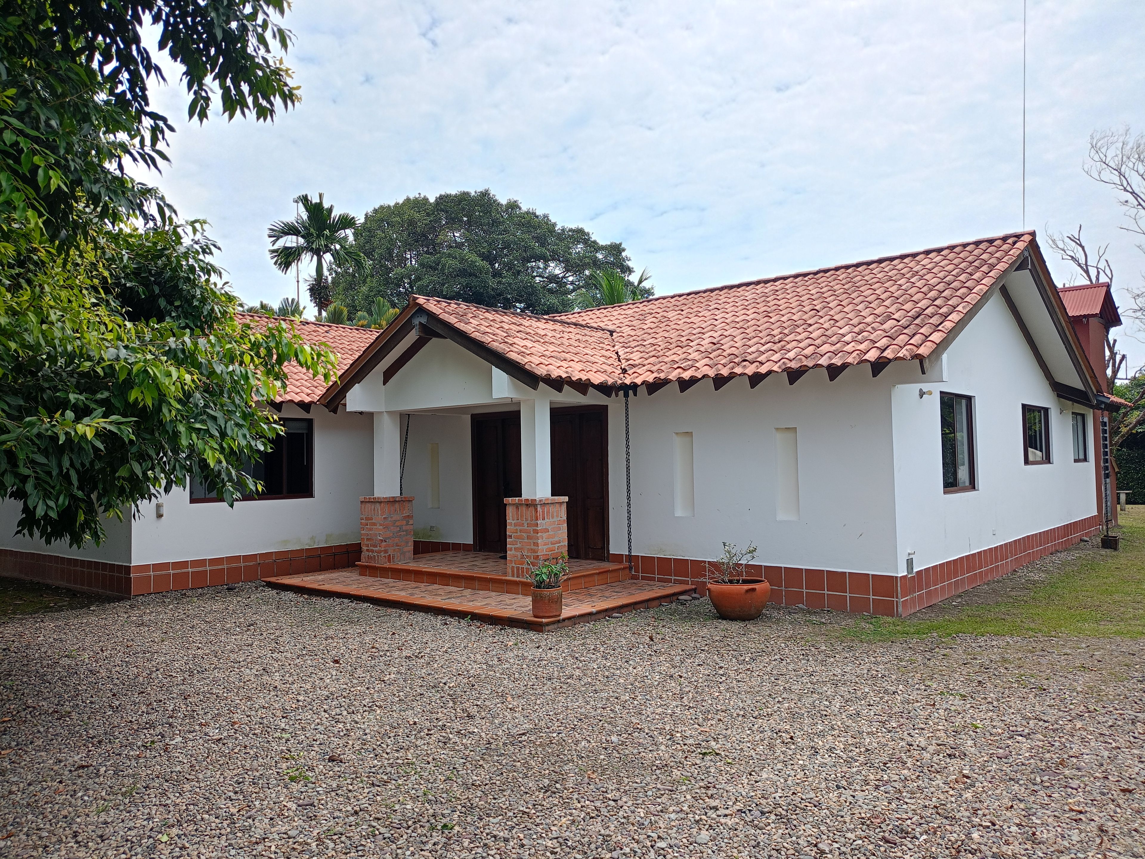 A single-story house with a tiled roof, a front porch, and a gravel driveway.